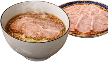 写真：醤油ラーメンの上に大判のチャーシューが2枚トッピングされている。別皿で薄切りのチャーシューだけが盛られている